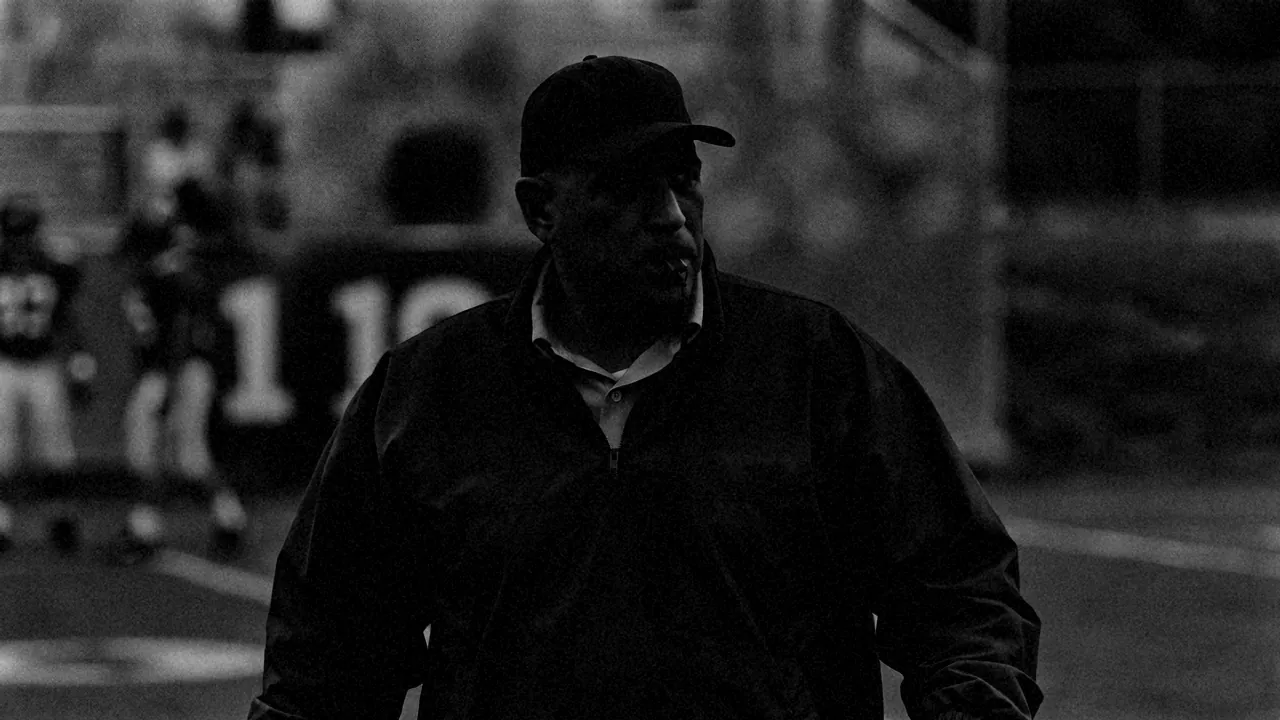 A coach on the sideline, whistle in his mouth, watching his team train.