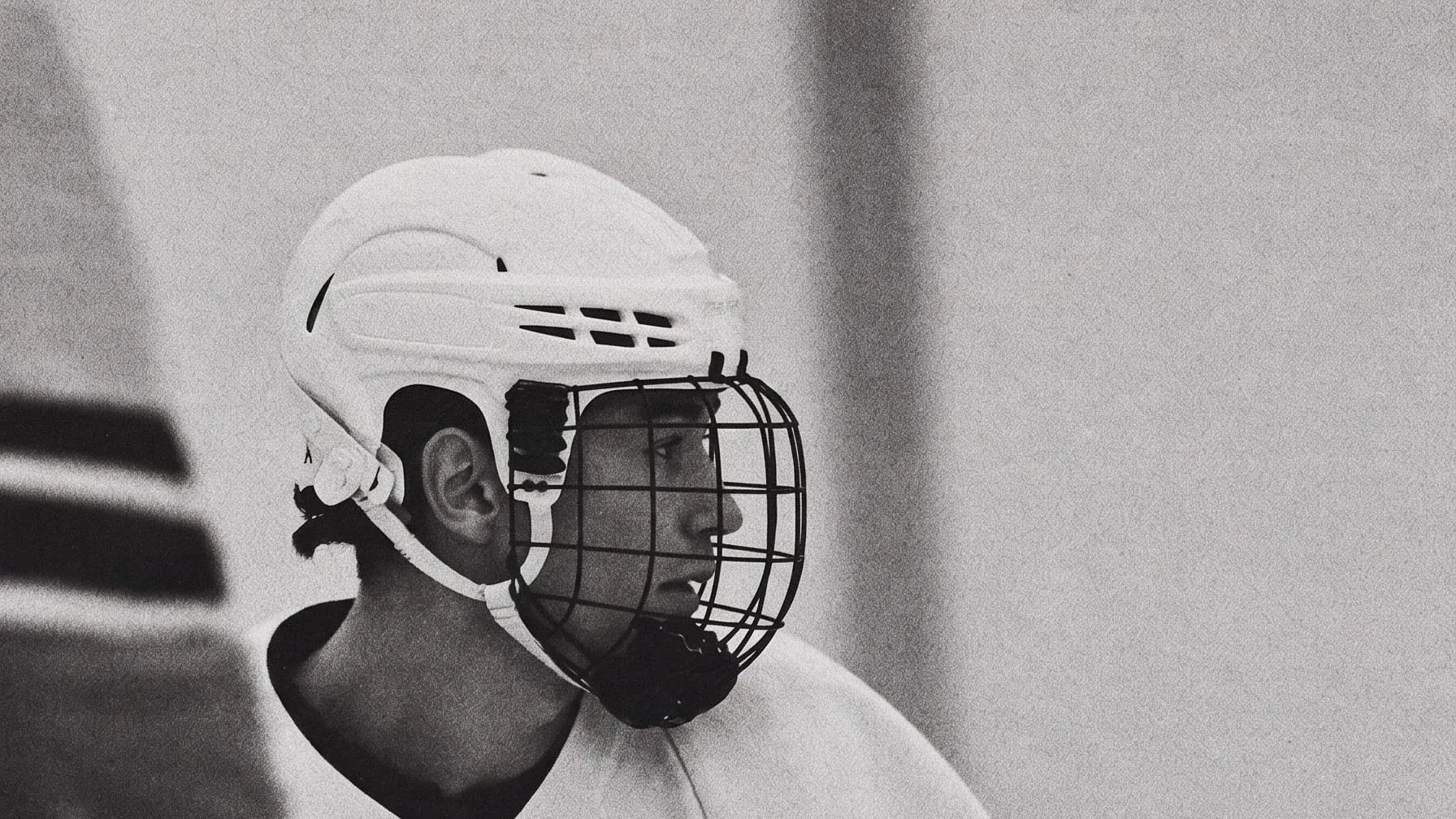 A hockey player in a white helmet and cage, watching the play
