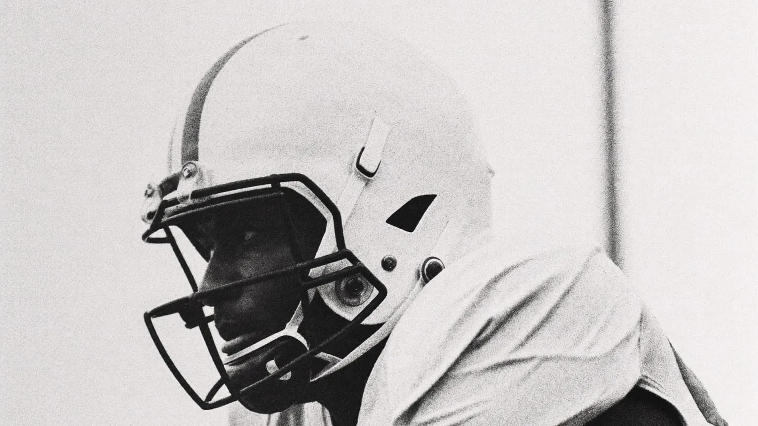 A football player in a white helmet, head down at the line