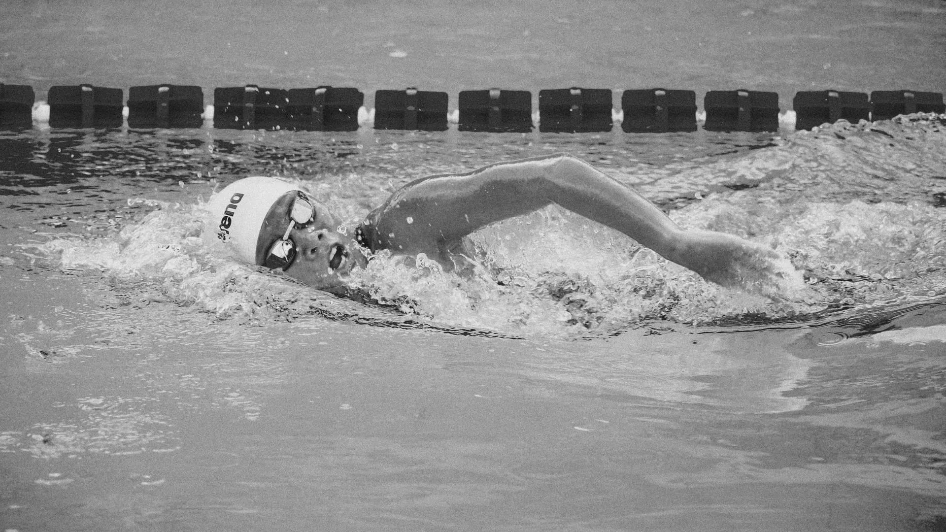 A freestyle swimmer mid-race, breathing beside the lane rope