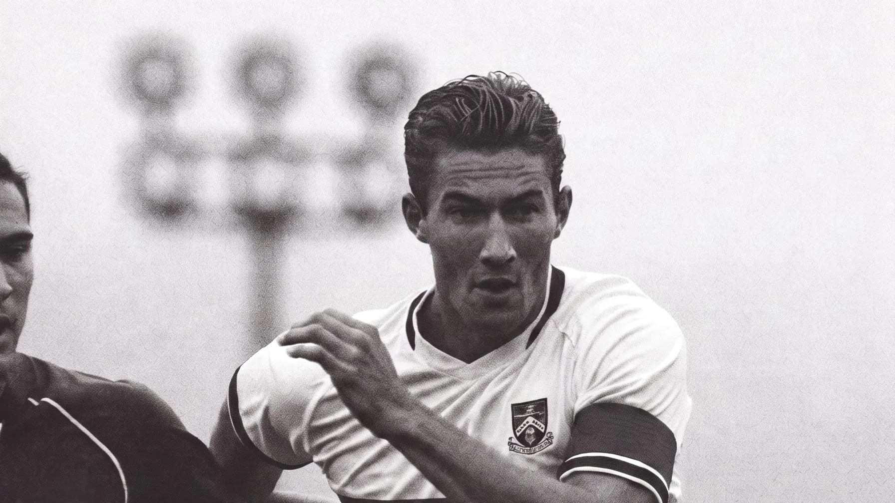 A soccer player driving forward under the floodlights, marked by a defender